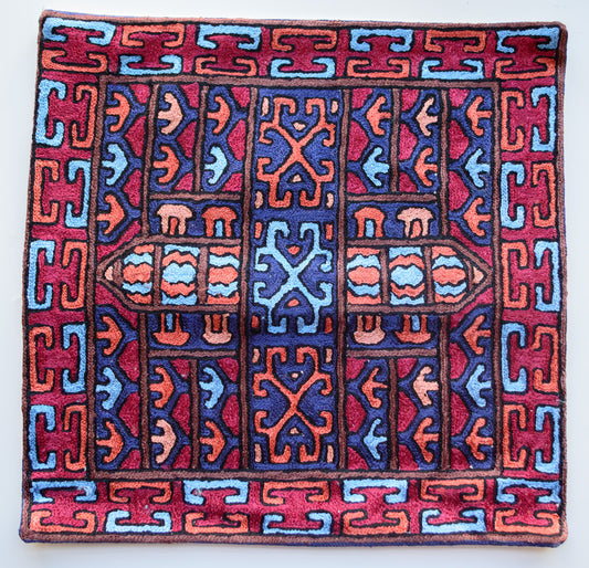 A close up cushion cover depicting a tribal pattern. This is an art silk cushion cover which is hand-embroidered by the artisans of Kashmir, India. The colors of the cushion are light brown, red, orange, light blue and dark blue.
