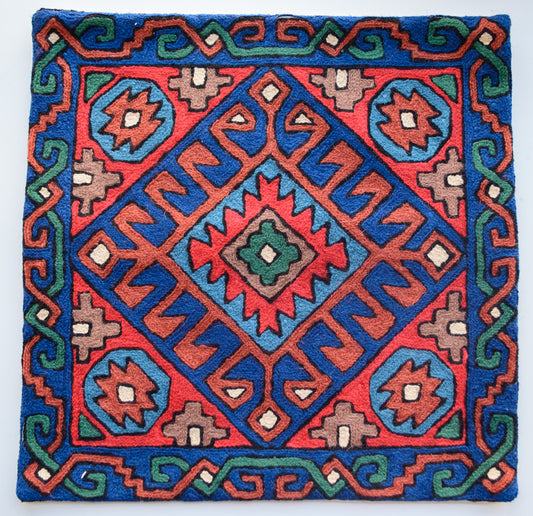 A close up cushion cover depicting a tribal pattern. This is a woolen cushion cover which is hand-embroidered by the artisans of Kashmir, India. The colors of the cushion are light brown, red, green, orange, light blue and dark blue.