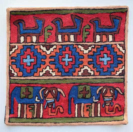 A close up cushion cover depicting a tribal pattern. This is a woolen cushion cover which is hand-embroidered by the artisans of Kashmir, India. The colors of the cushion are dark brown, light yellow, red, orange, green, light blue and dark blue.