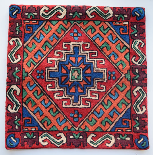 A close up cushion cover depicting a tribal pattern. This is an wool cushion cover which is hand-embroidered by the artisans of Kashmir, India. The colors of the cushion are dark brown, red, orange, green and dark blue.