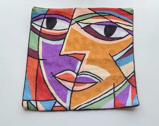 A close up cushion cover showing the face design created by the famous painter Picasso. Its a colorful cushion with many colors. You can see the eyes, nose, cheeks and lip of the face clearly. The colors of the cushion are black for the eye pupil, yellow, purple, red, orange, green, blue and brown.