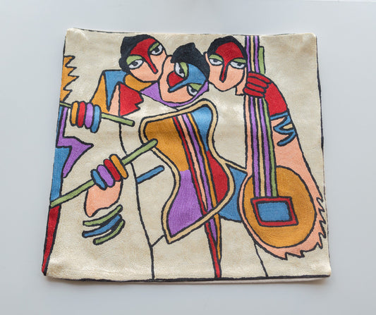 A close up cushion showing showing the 3 musicians playing the maracus, violin and guitar. The design is inspired by famous painters Alfred Gockel and Picasso. The background is light yellow color. The colors of the musicians and instruments are red, black for their hair, cream, purple, yellow and blue.
