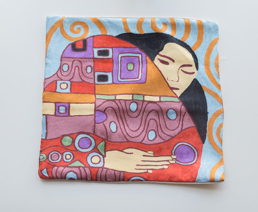 A close up cushion cover depicting the design of a woman holding her mountain of creativity on her sleeve. Ths design is inspired by famous pianters Alfred Gockel and Picasso. It is a vivid design with many colors. The woman's hair is black, she has light yellowish color skin, the backdrop is light blue with orange spiral like design. There are geometric shapes on her sleeve and the colors are brown, blue, purple, red, yellow and green.