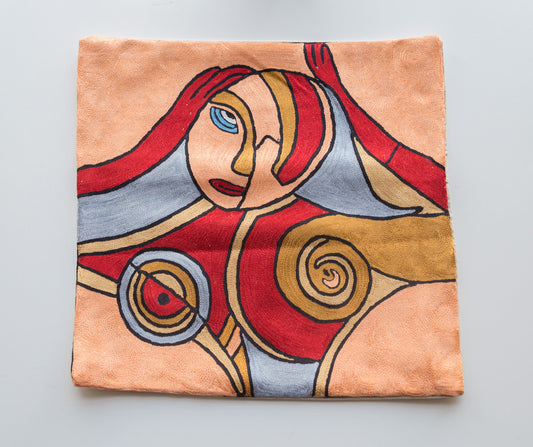 A close up cushion cover depicting an art form of a woman inspired by famous painters Alfred Gockel and Picasso. The background color is light orange. The woman depicted has her face and upper body and hands shown. The colors of the woman are grey, red, light orange, and brown. 