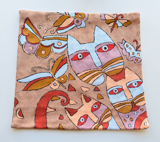 A close up cushion cover with the design of 3 cats and 5 butterflies on a brown background. The cats faces are seen in the design. The main colors of the cats and butterflies rae brown, blue, red, lavender and cream.