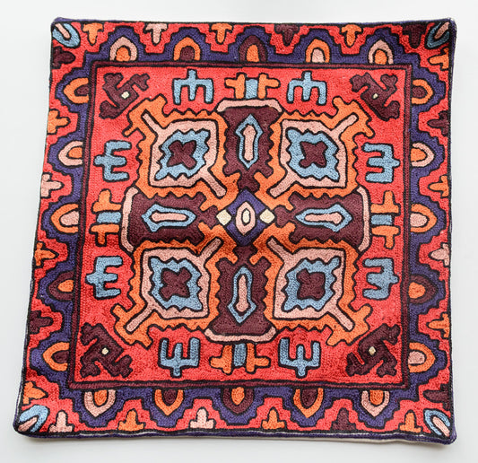 A close up cushion cover depicting a tribal pattern. This is an art silk cushion cover which is hand-embroidered by the artisans of Kashmir, India. The colors of the cushion are dark brown, red, orange, dark purple and light blue.